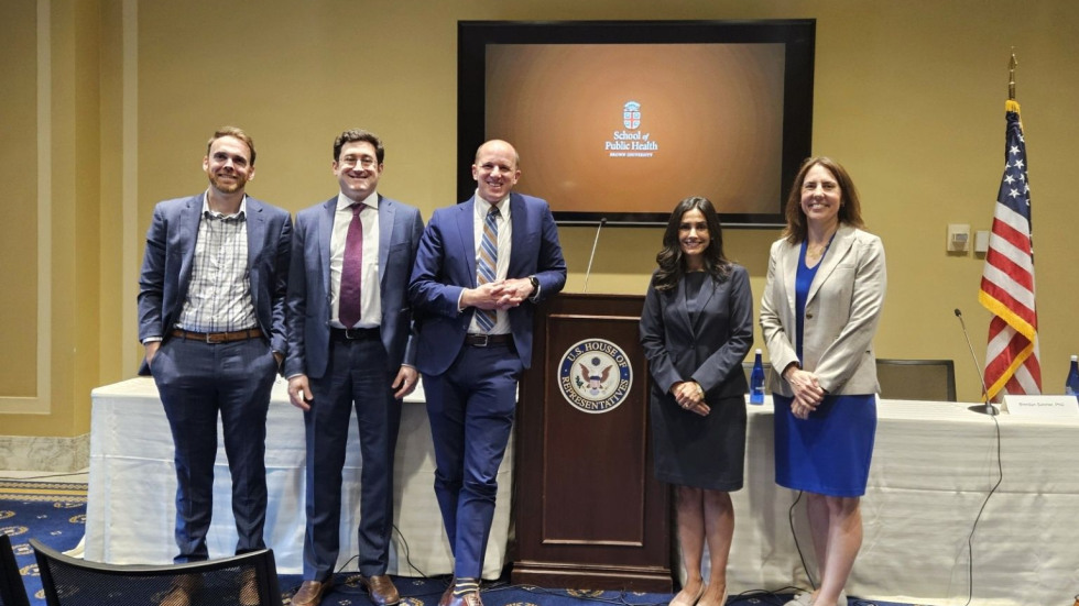 Jared Perkins, Dr. Michael Barnett, Brendan Saloner, Dr. Yashaswini Singh, and Dr. Francesca Beaudoin stand in a row beside a wooden podium marked with the U.S. House of Representatives seal, smiling for a group photo.